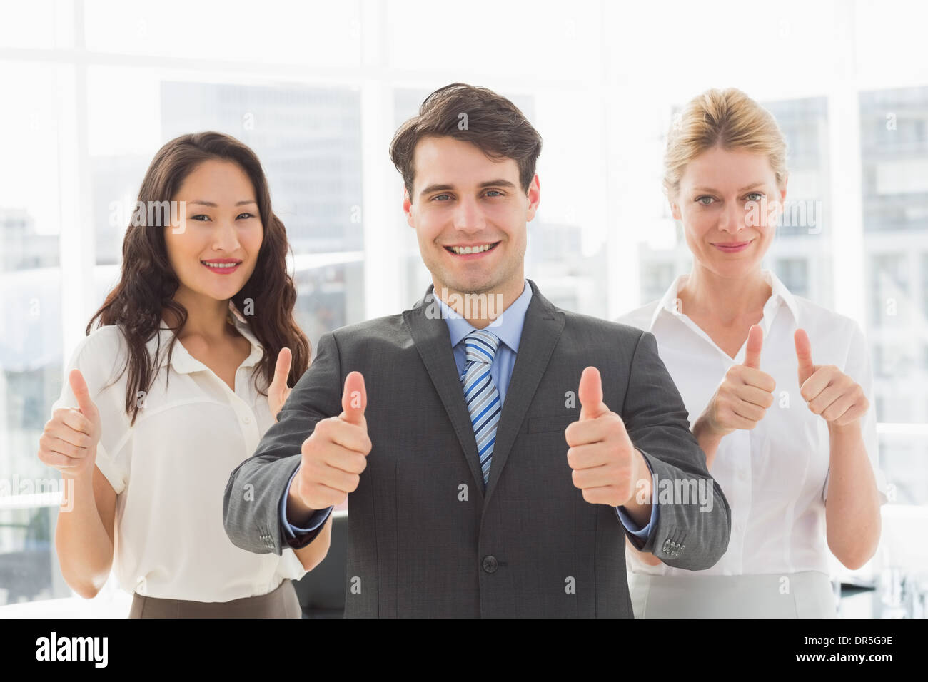 Smiling businessman giving thumbs up with his team Stock Photo - Alamy