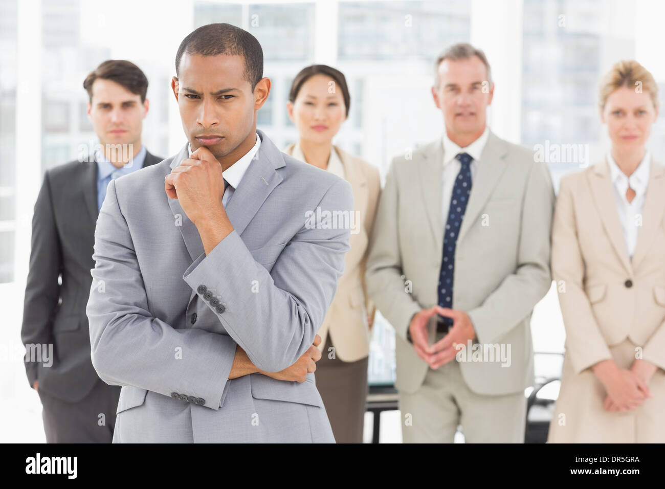 Serious businessman frowning at camera with team behind him Stock Photo ...