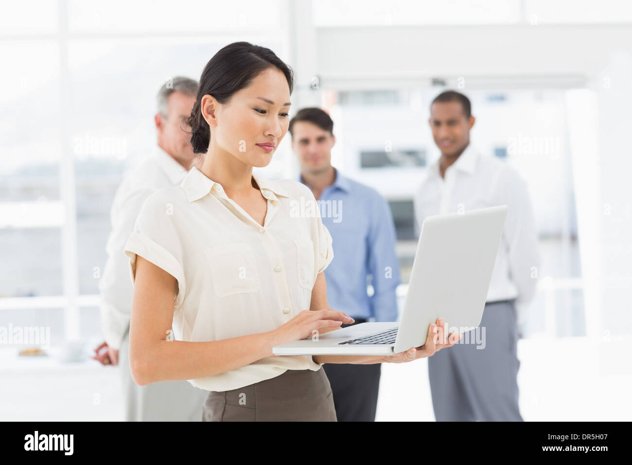 Pretty asian businesswoman using laptop with team behind her Stock Photo