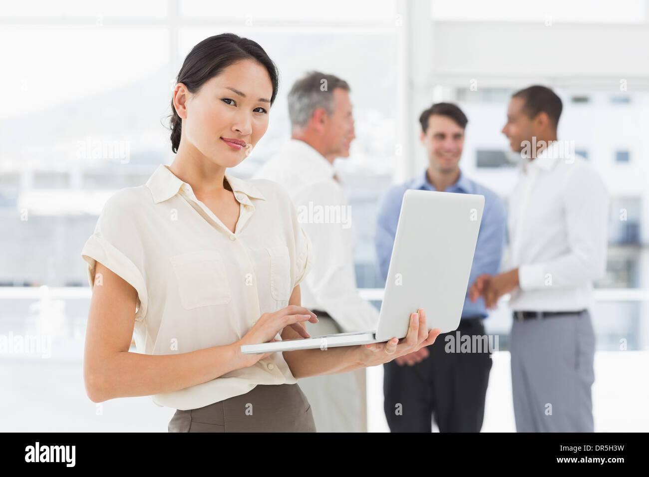 Asian businesswoman using laptop with team behind her Stock Photo