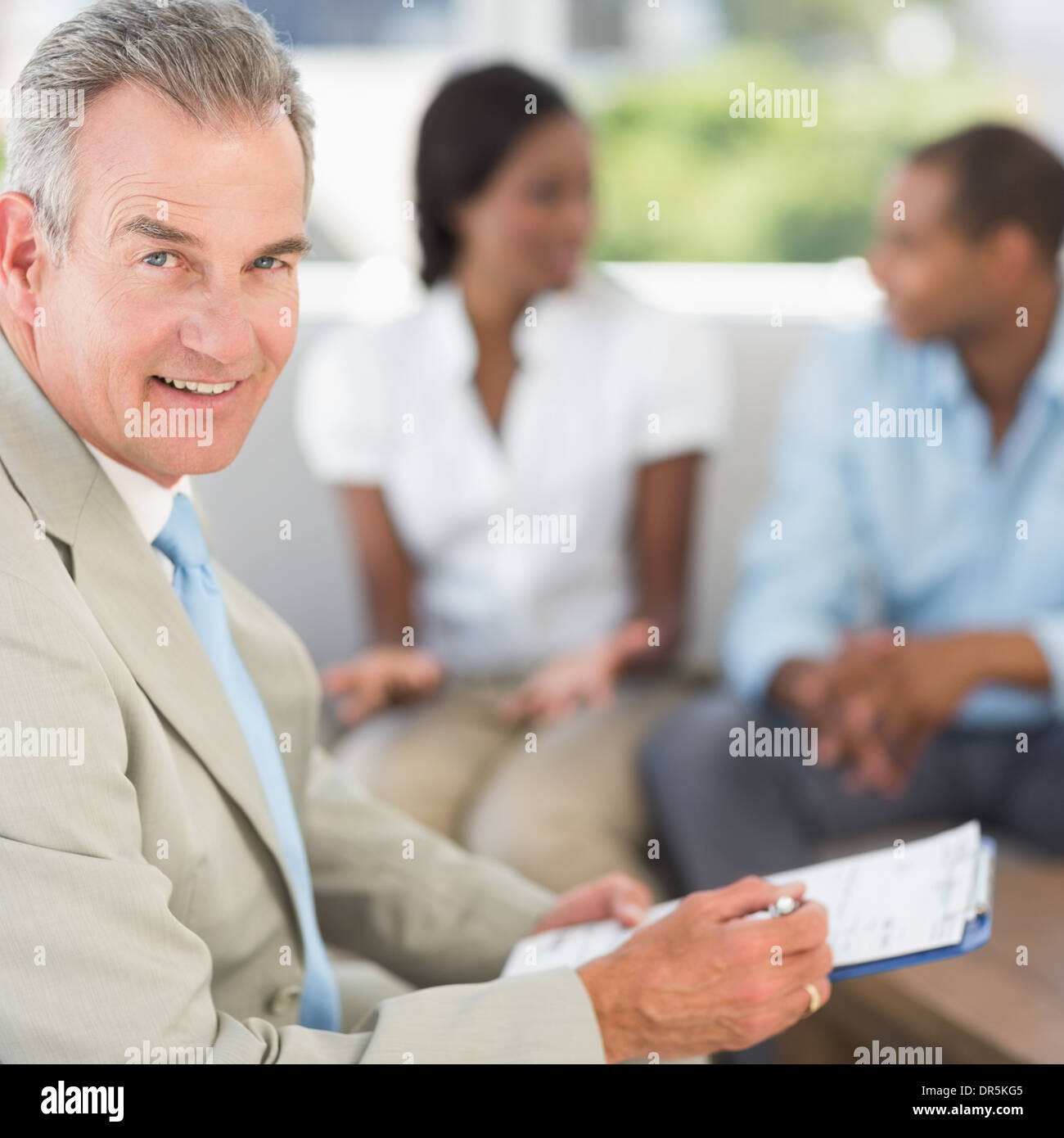 Salesman smiling at camera with couple behind him Stock Photo - Alamy