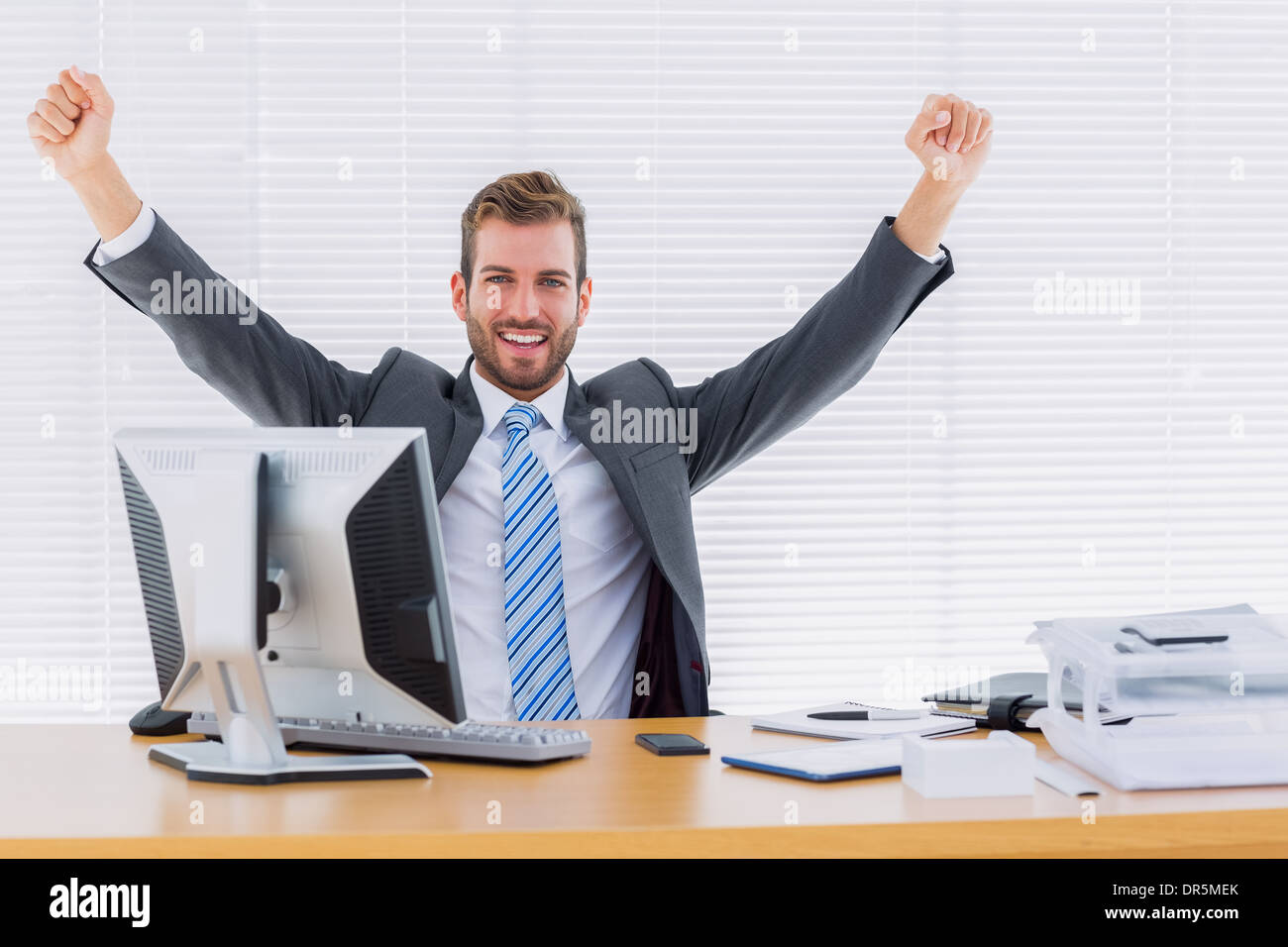 Cheerful businessman clenching fist at office desk Stock Photo