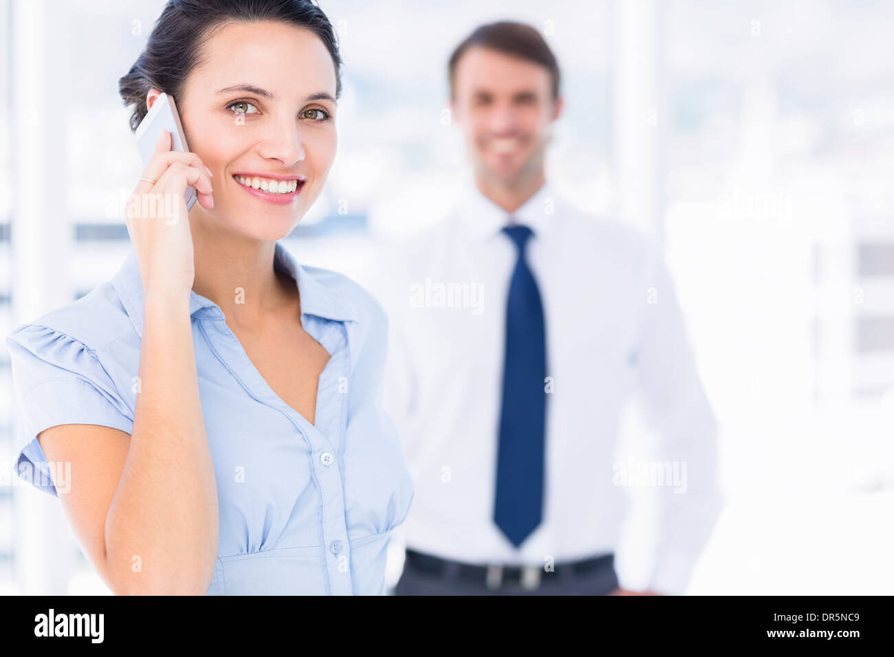 Woman on call with male colleague in background Stock Photo
