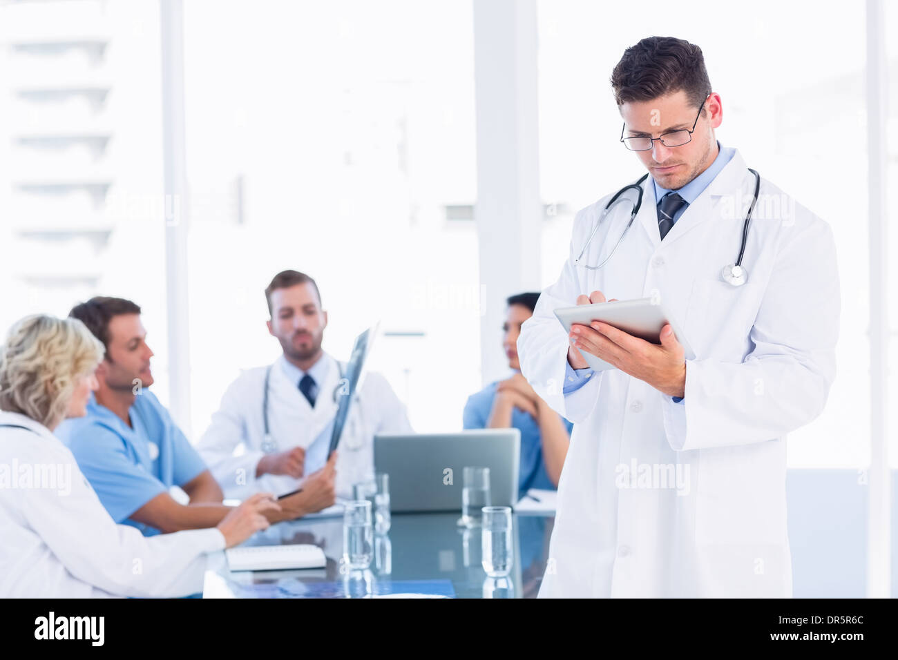 Doctor using digital tablet with colleagues in meeting Stock Photo