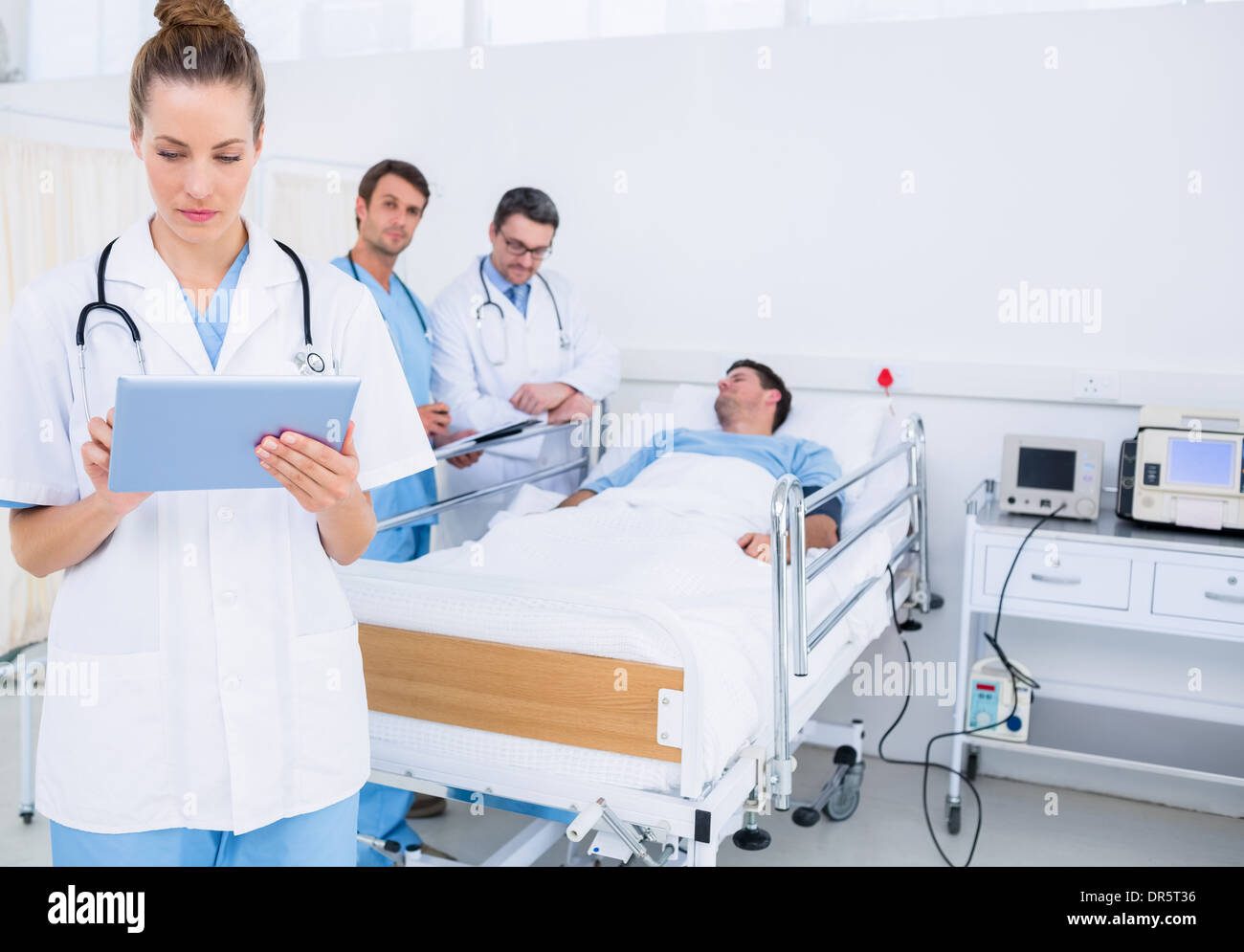 Doctor using digital tablet with colleagues and patient behind Stock Photo