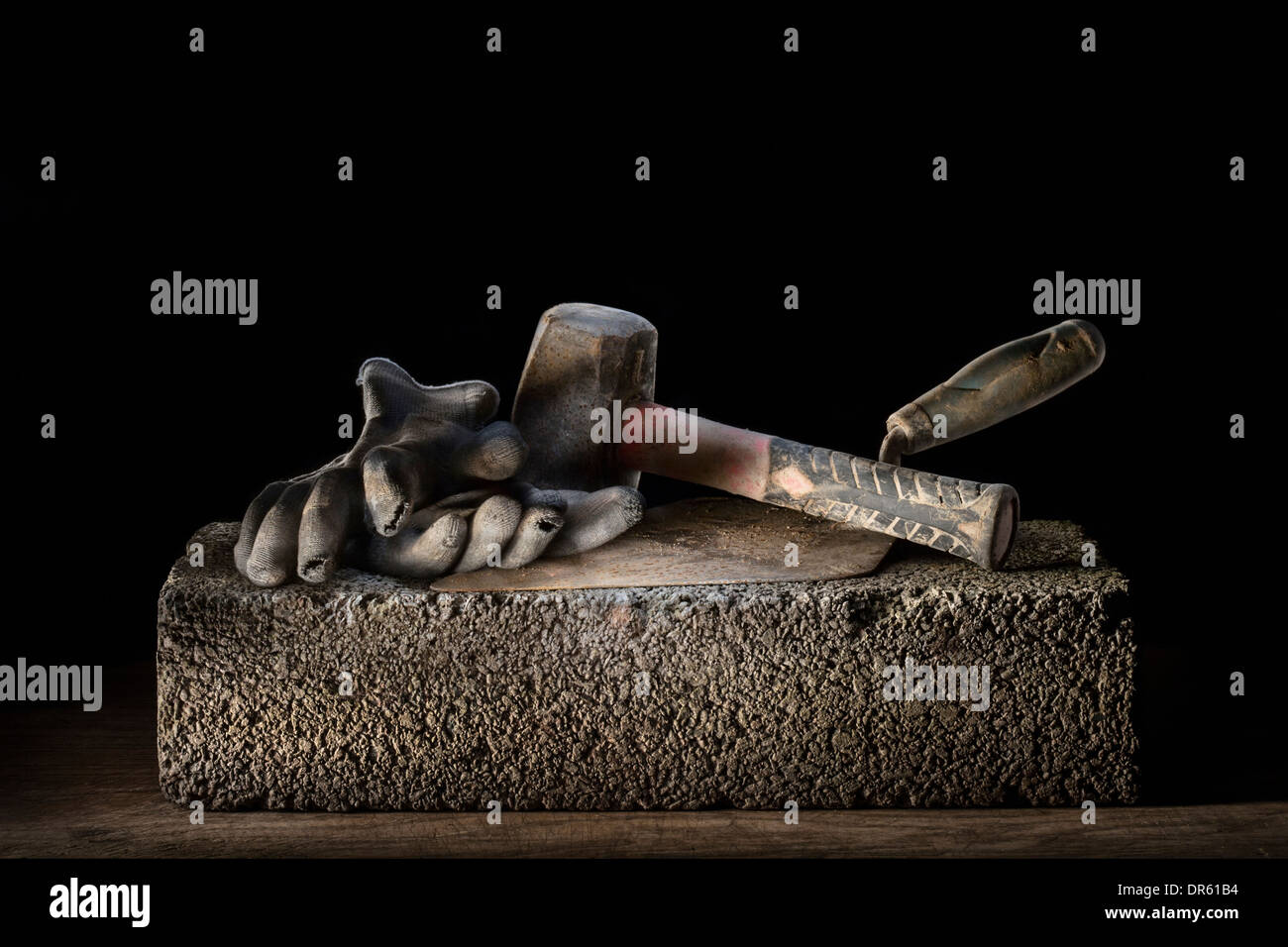 Builder's lump hammer, gloves and trowel resting on a concrete block. Stock Photo