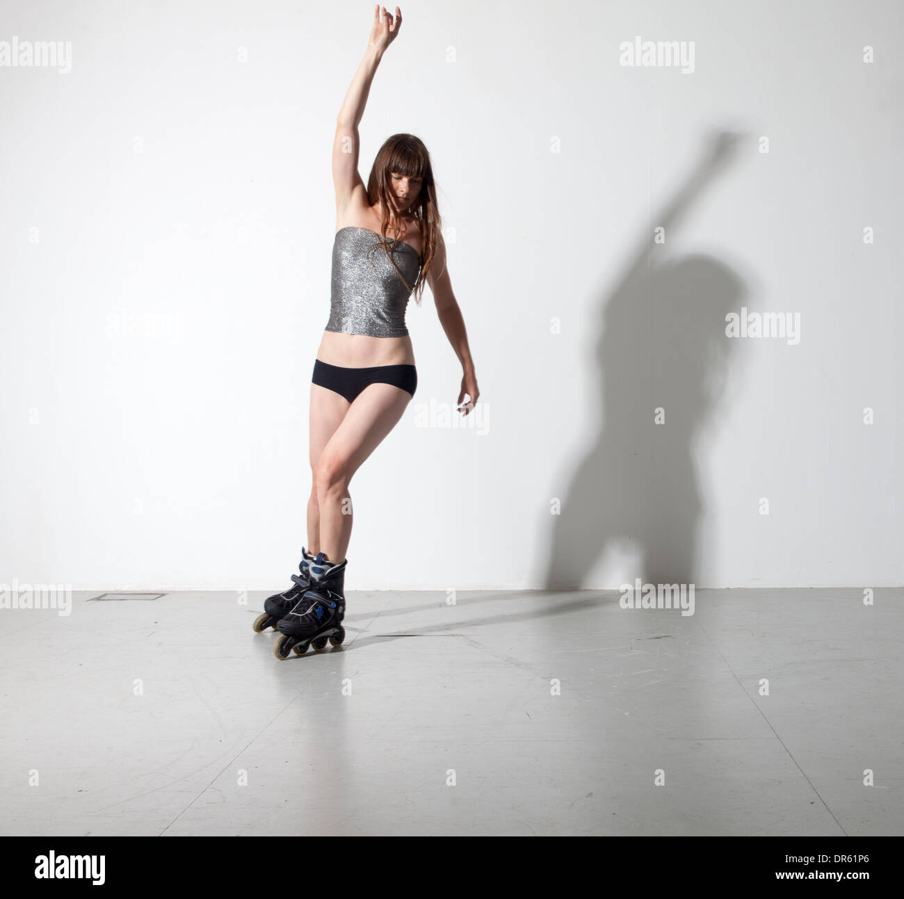 woman roller blading, long hair, skating , silver top, arm up, shadow Stock Photo