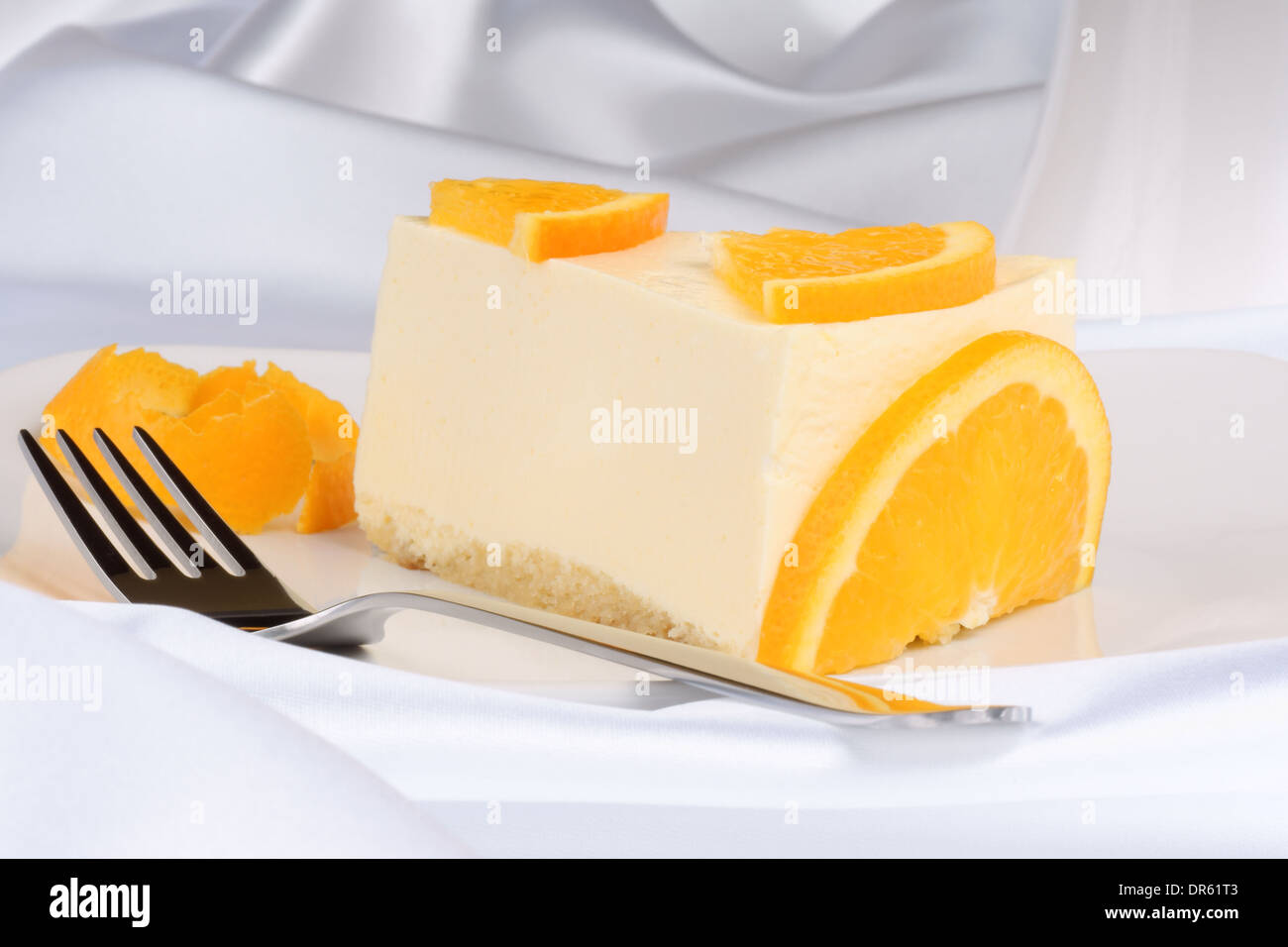 Slice of orange bavarian cream (bavarese) and a dessert fork on a white porcelain dish Stock Photo