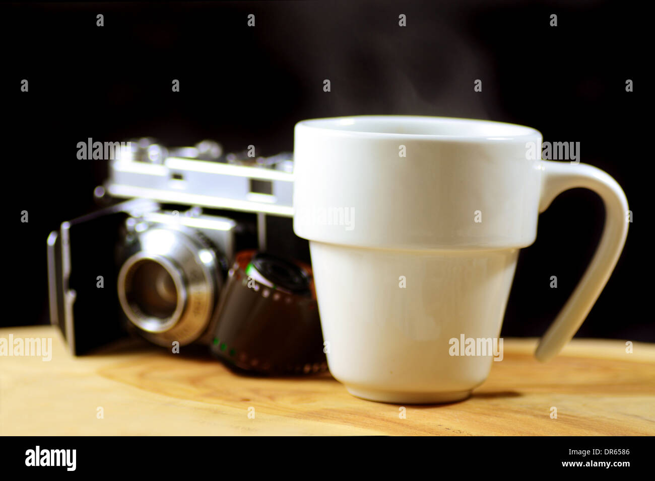 Macro shot of a steaming cup of coffee with an analog camera and roll of film in the background Stock Photo