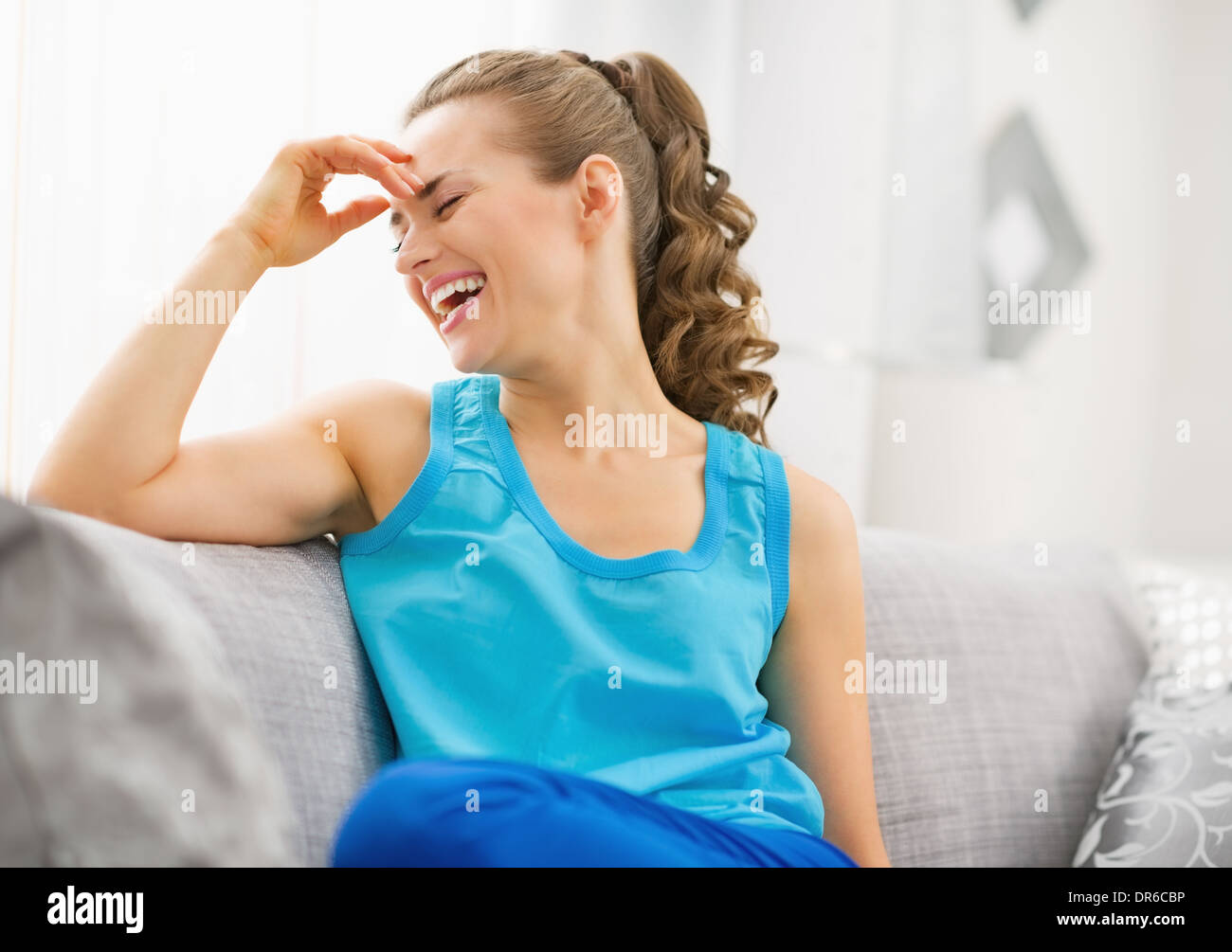 Young woman sitting on sofa and laughing Stock Photo - Alamy