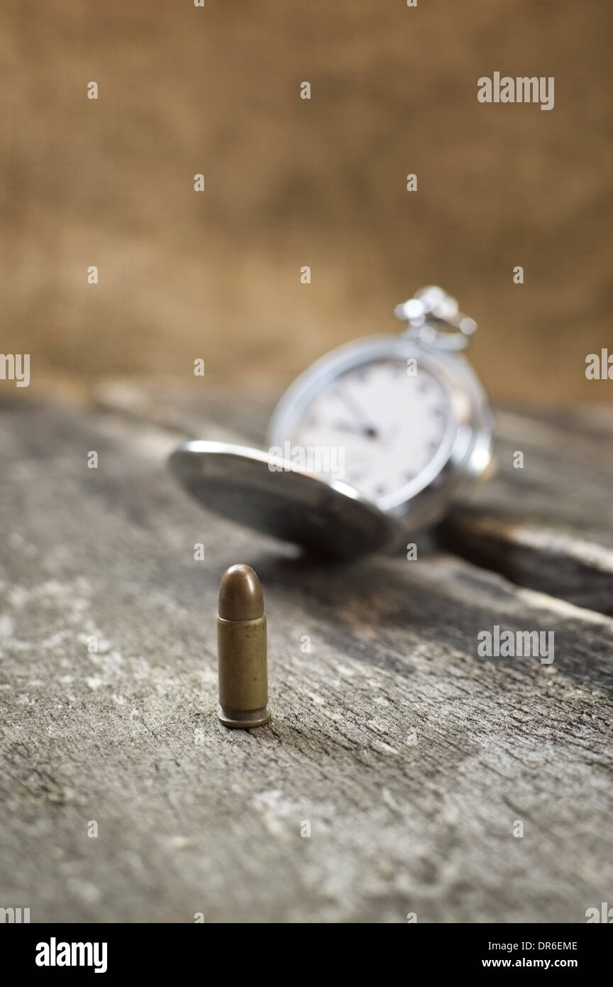 Bullet on wooden table with old pocket watch. Selective focus on bullet. Stock Photo