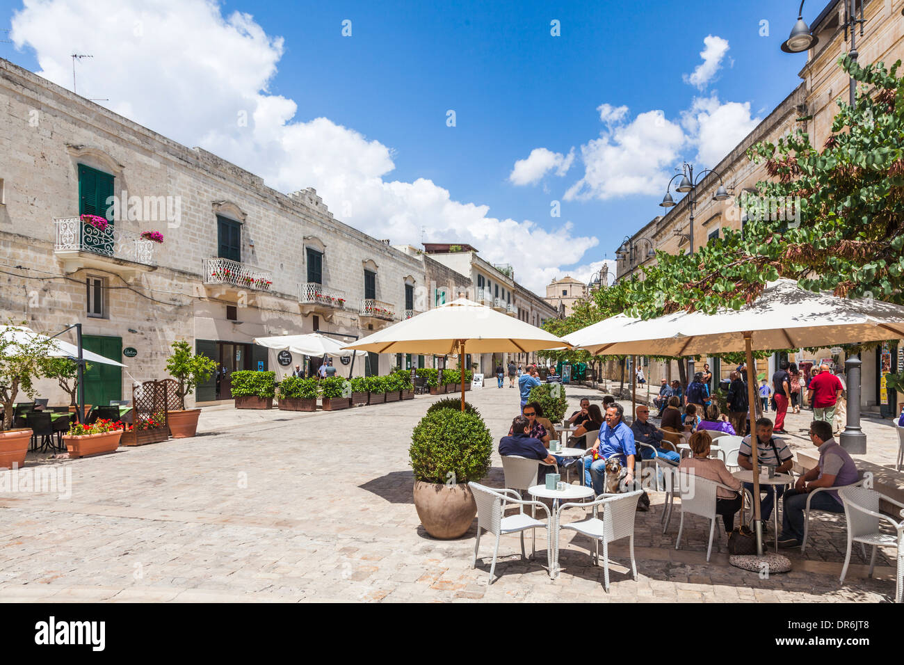 Tourists enjoying pavement cafes under umbrellas in Via D. Pascoli, Matera, Basilicata, southern Italy on a sunny summer day under a blue sky Stock Photo