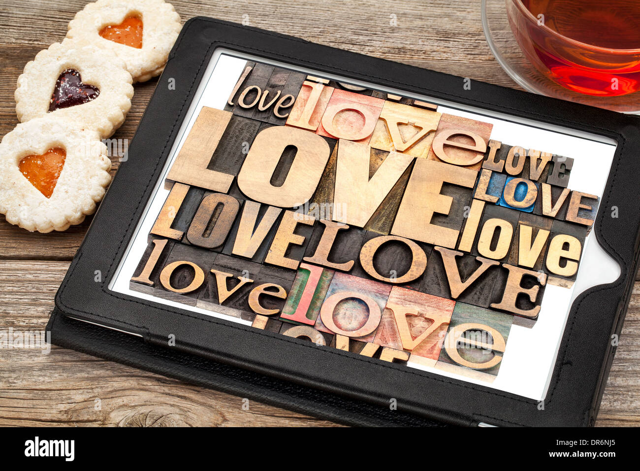 love word abstract - in vintage letterpress wood type printing blocks on a digital tablet with cup of tea and heart cookies Stock Photo