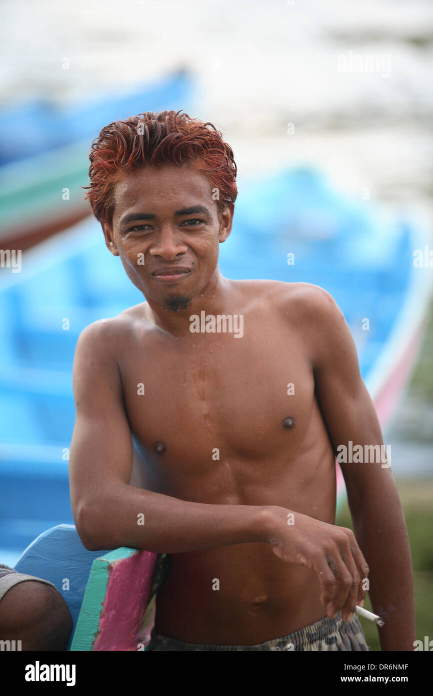 Portrait of a smiling Indonesian young man smoking cigarette in boatyard looking at camera Kupang, West Timor, Indonesia Stock Photo