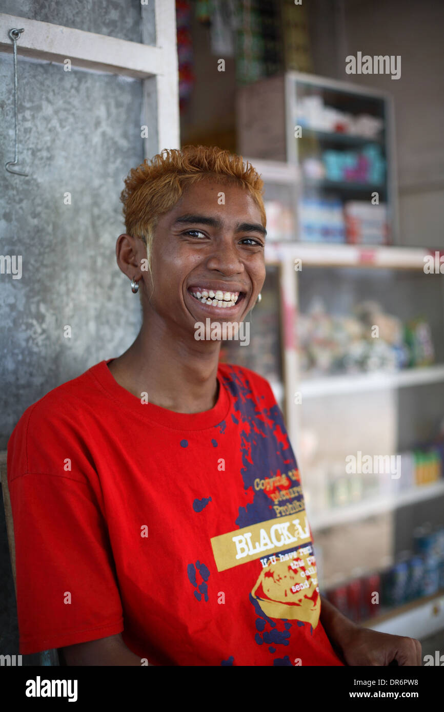Smiling Indonesian teen boy / young adult vendor with earings, red hair and red t-shirt. Kupang, West Timor, Indonesia Stock Photo