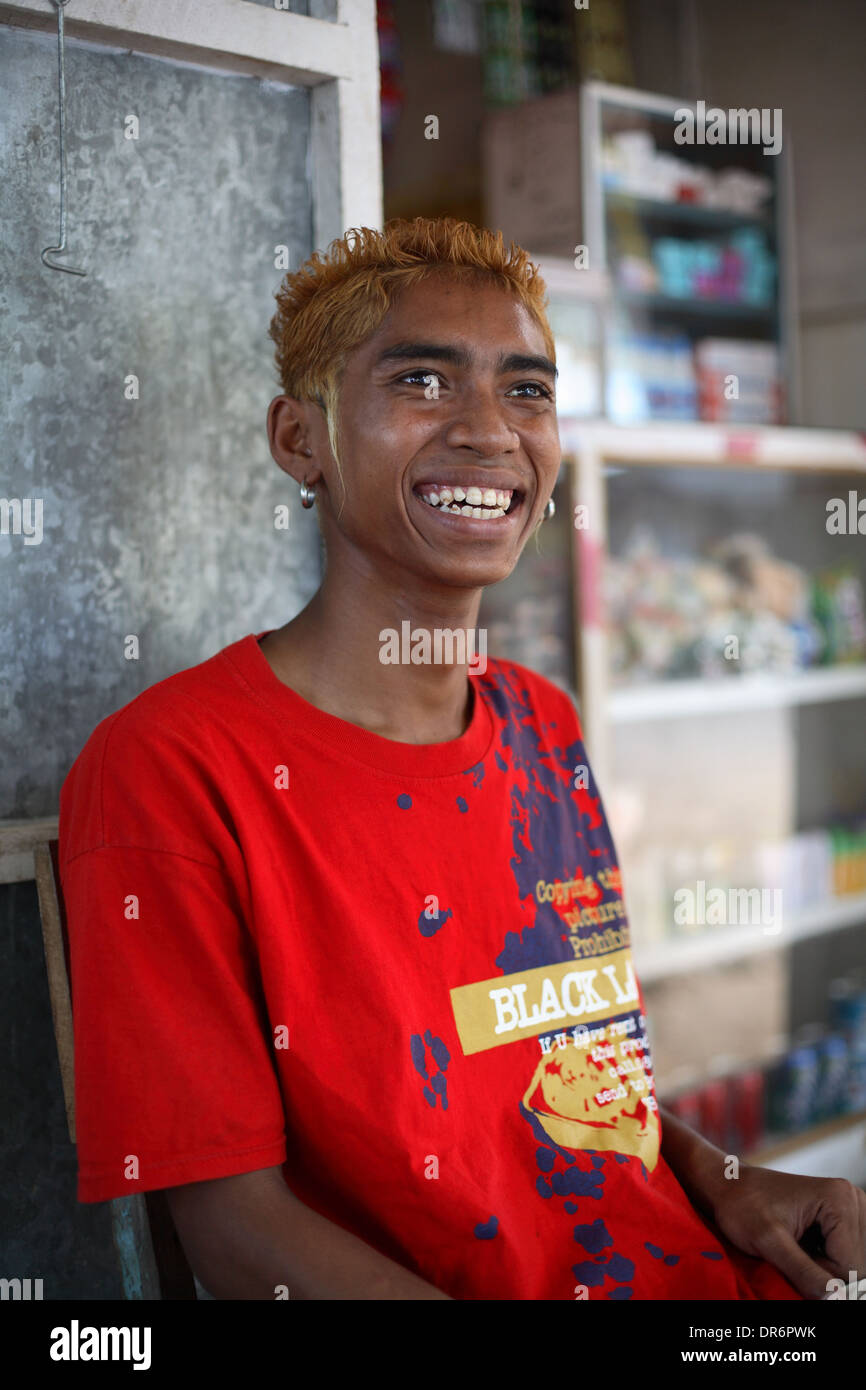Smiling Indonesian teen boy / young adult vendor with earings, red hair and red t-shirt. Kupang, West Timor, Indonesia Stock Photo