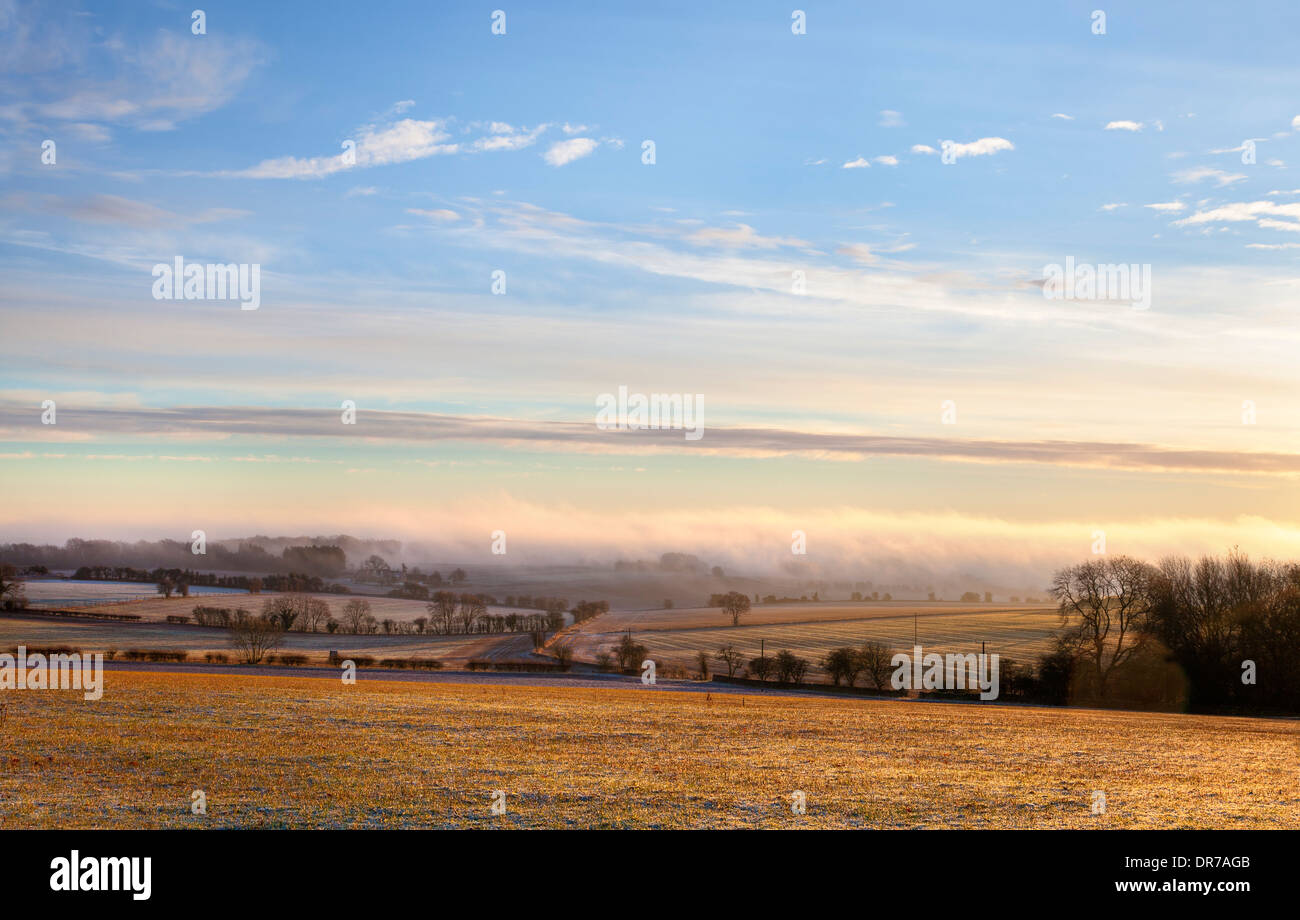 Cold winters morning with the sun shining through the mist over arable farmland, Gloucestershire, England. Stock Photo