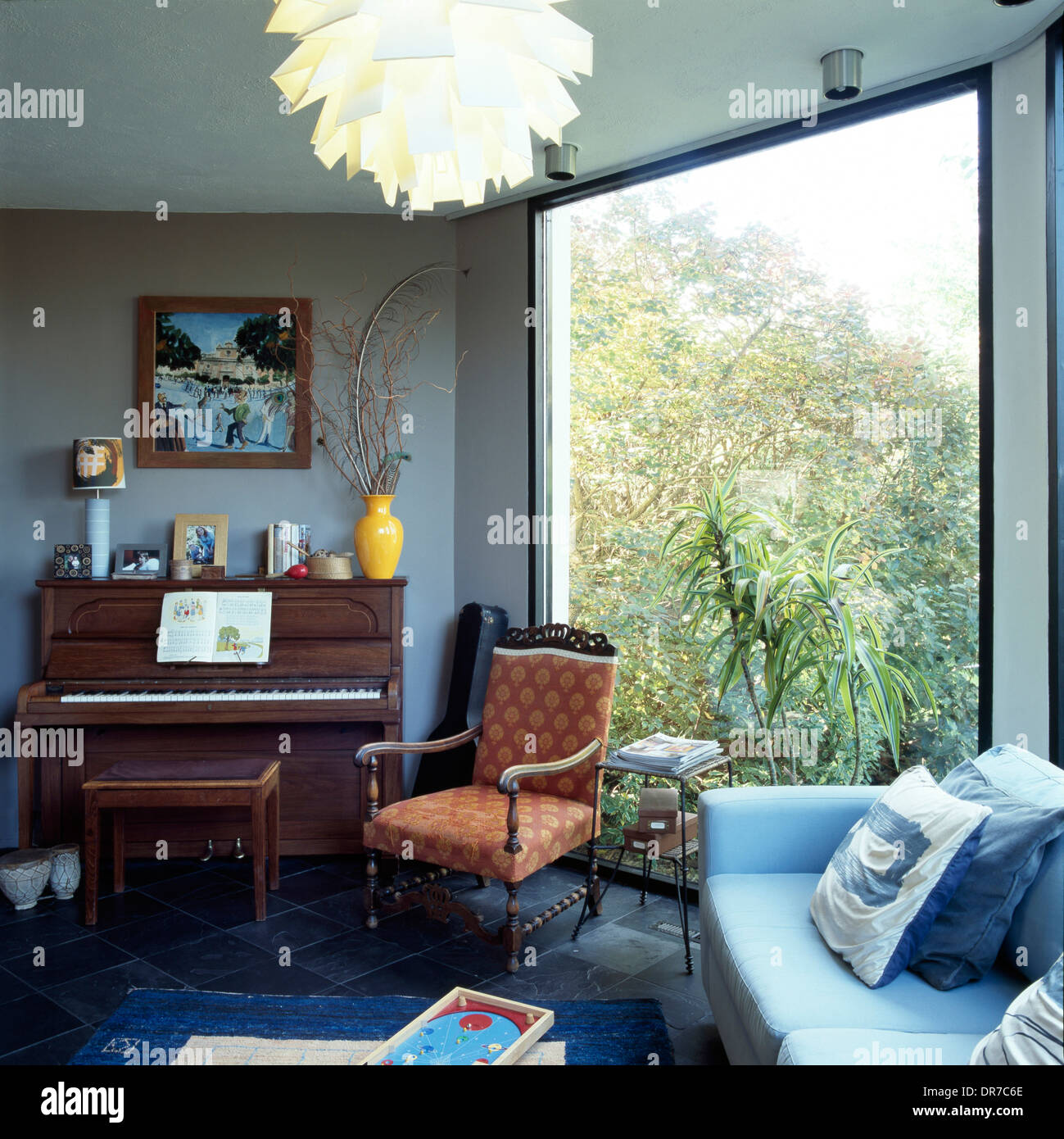 Family room with upright piano next to full height window Stock