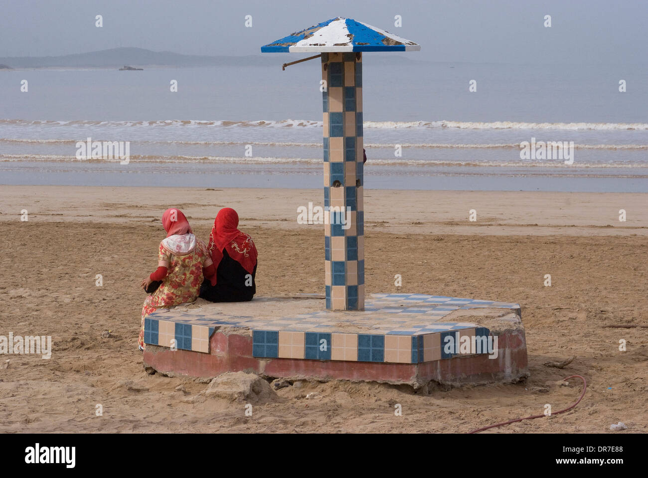 Traditionally dressed women enjoying watching the waves on the beach, Essaouira, Morocco Stock Photo