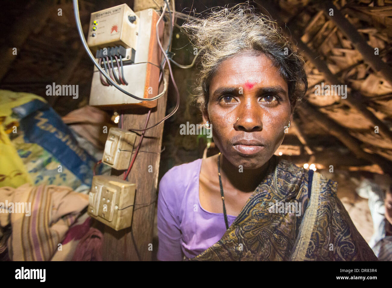 An untouchable woman in her hut, illuminated by an electric light, powered by an A4 sized solar panel, that charges a battery, and enables her to have light. The prrject was sponsored by the Rotary club. Before the installation of the solar panels, the houses would be lit by kerosene lamps. Over 1 million women and children die every year in india from inhaling kerosene fumes. Stock Photo