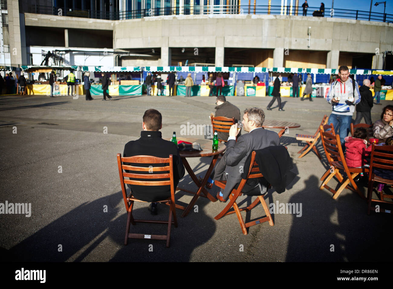 Two men relaxing outdoors drinking beer looking at market stalls at Canary Wharf. Stock Photo