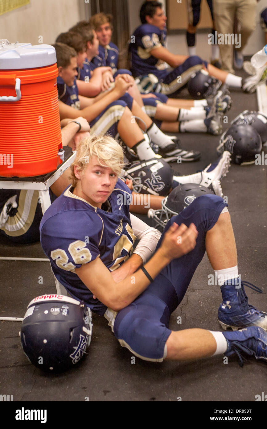 A blonde high school football player relaxes in the locker room during
