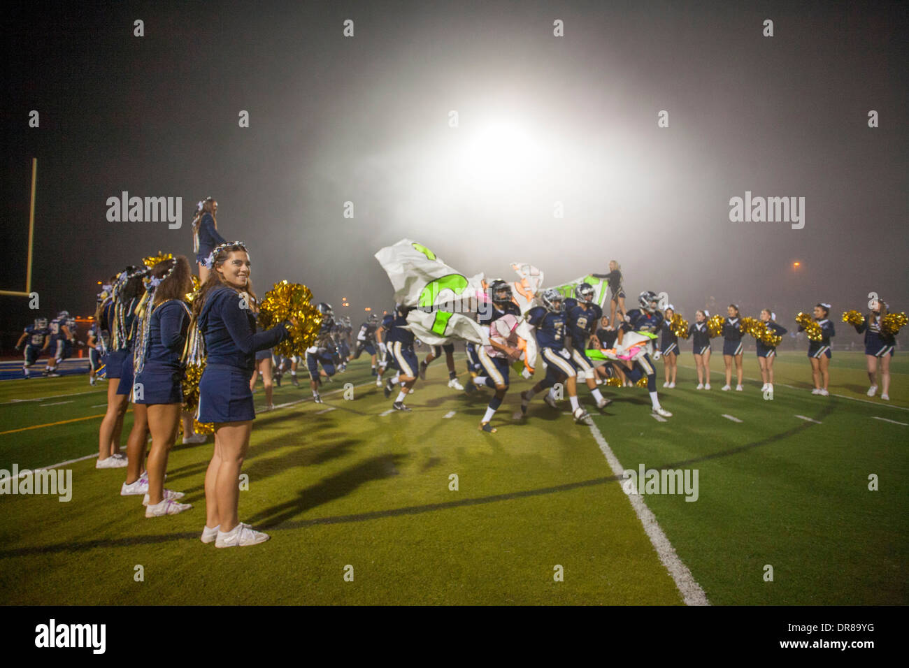 High school football football players run through an inspirational banner held by cheerleaders at the start of a night game in San Juan Capistrano, CA. Stock Photo