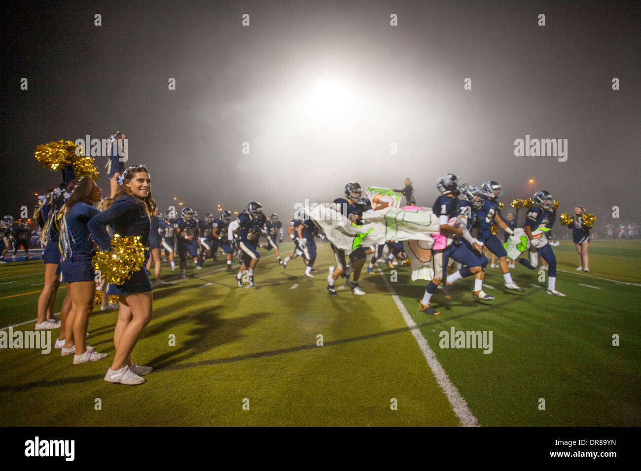 High school football football players run through an inspirational banner held by cheerleaders at the start of a night game in San Juan Capistrano, CA. Stock Photo
