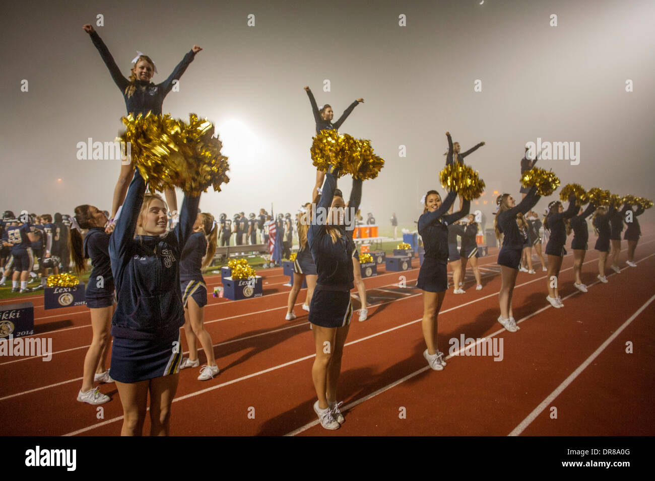 Cheerleaders entertain the spectators at a high school night football game in San Juan Capistrano, CA, hold initials of the school name. Note 'flyers' on shoulders of other cheerleaders. Stock Photo