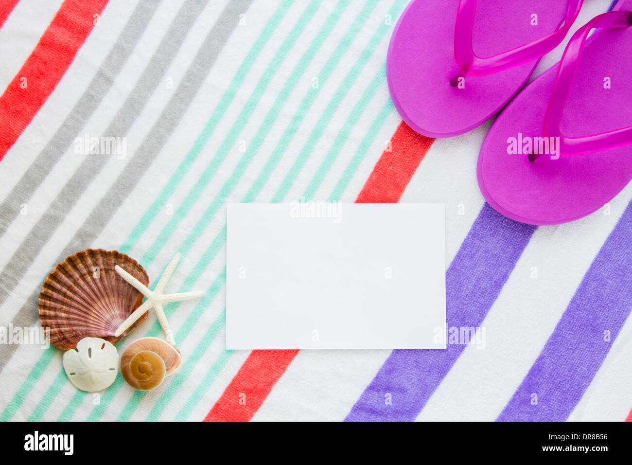 Beach scene with purple flip flops, shells, starfish, and a sand dollar on a striped beach towel with copy space. Stock Photo