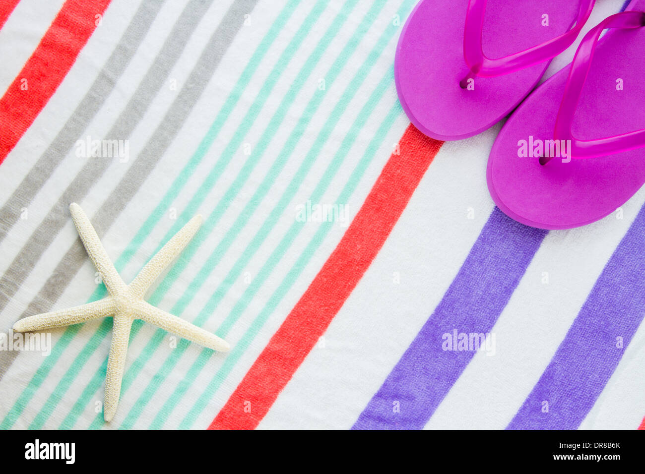 Beach scene with purple flip flops and a starfish on a striped beach towel. Stock Photo