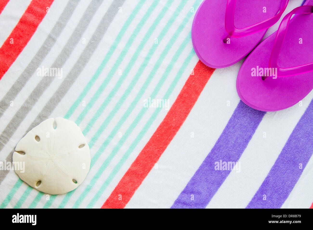Beach scene with purple flip flops and a sand dollar on a striped beach towel. Stock Photo