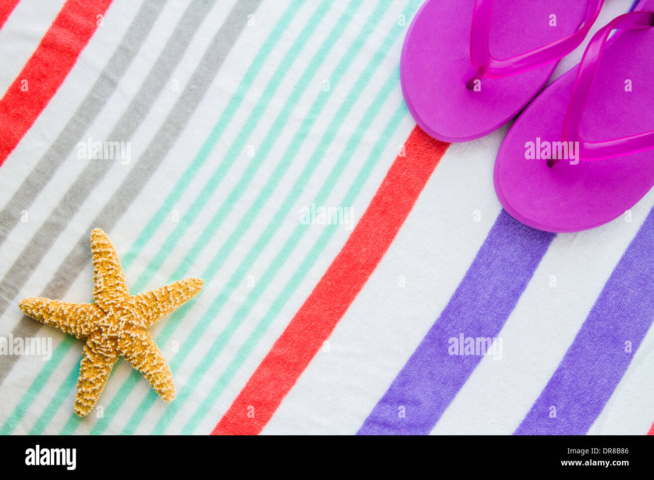 Beach scene with purple flip flops and a starfish on a striped beach towel. Stock Photo