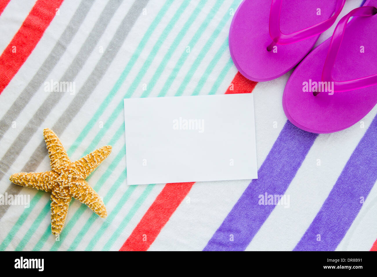 Beach scene with purple flip flops and a starfish on a striped beach towel with copy space. Stock Photo