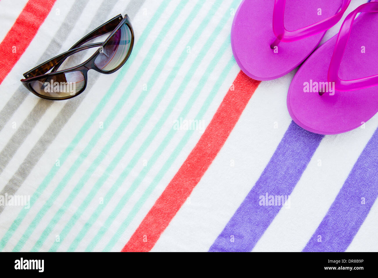 Beach scene with purple flip flops and sunglasses on a striped beach towel. Stock Photo