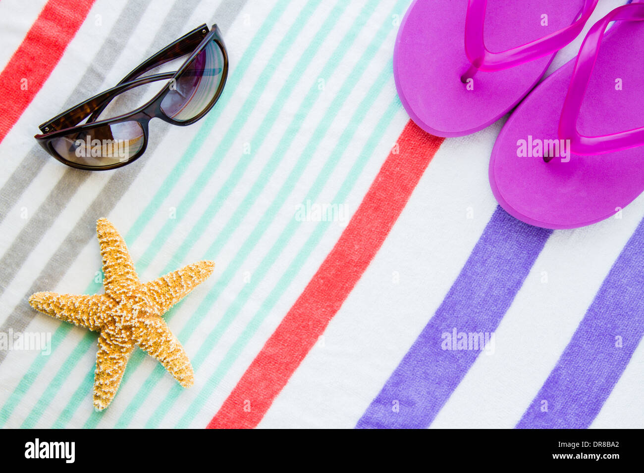 Beach scene with purple flip flops, sunglasses and a starfish on a striped beach towel. Stock Photo