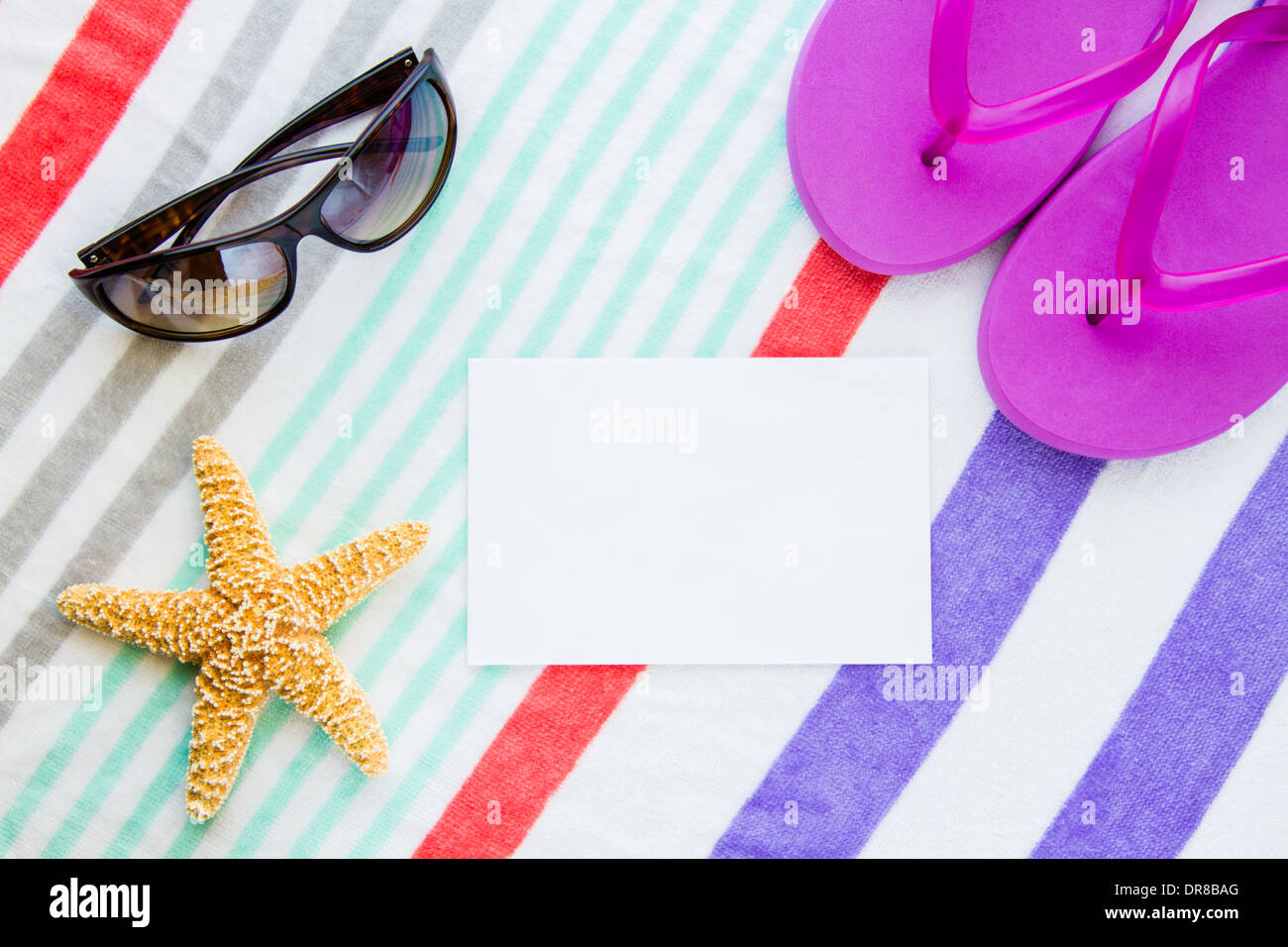 Beach scene with purple flip flops, a starfish, and sunglasses on a striped beach towel with copy space. Stock Photo