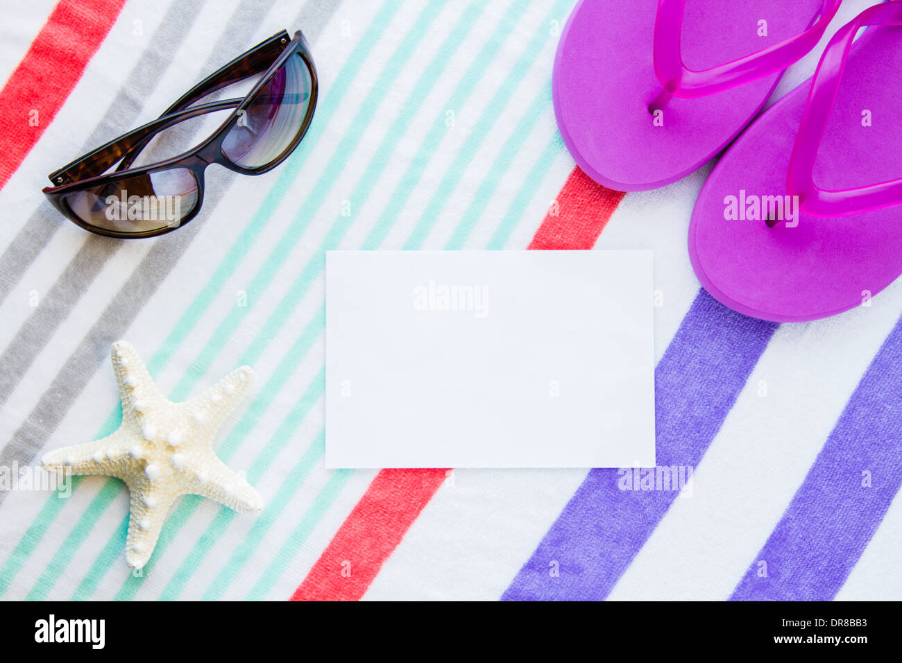 Beach scene with purple flip flops, a starfish, and sunglasses on a striped beach towel with copy space. Stock Photo