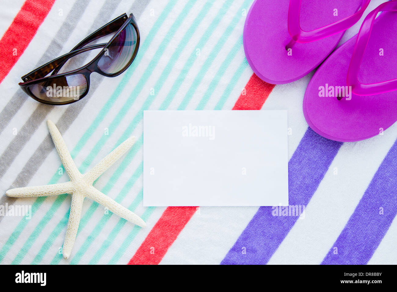 Beach scene with purple flip flops, a starfish, and sunglasses on a striped beach towel with copy space. Stock Photo