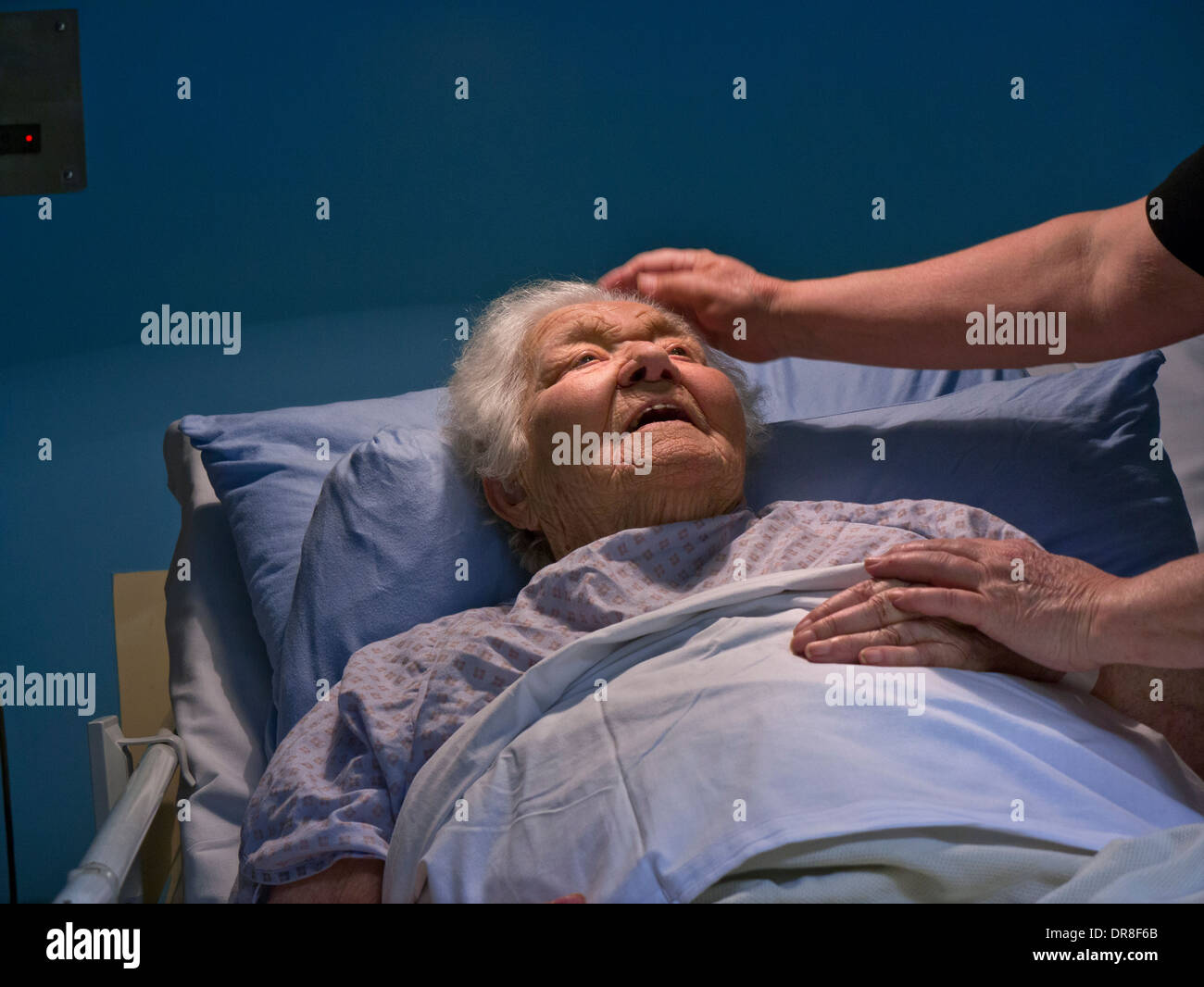 Contented smiling senior old age elderly lady in hospital bed with comforting hand of carer nurse Stock Photo