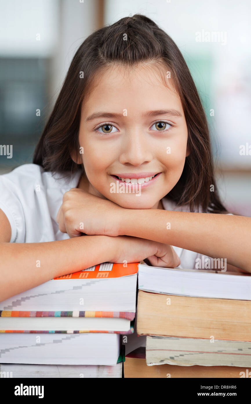 Schoolgirl Leaning On Stack Of Books In Classroom Stock Photo - Alamy