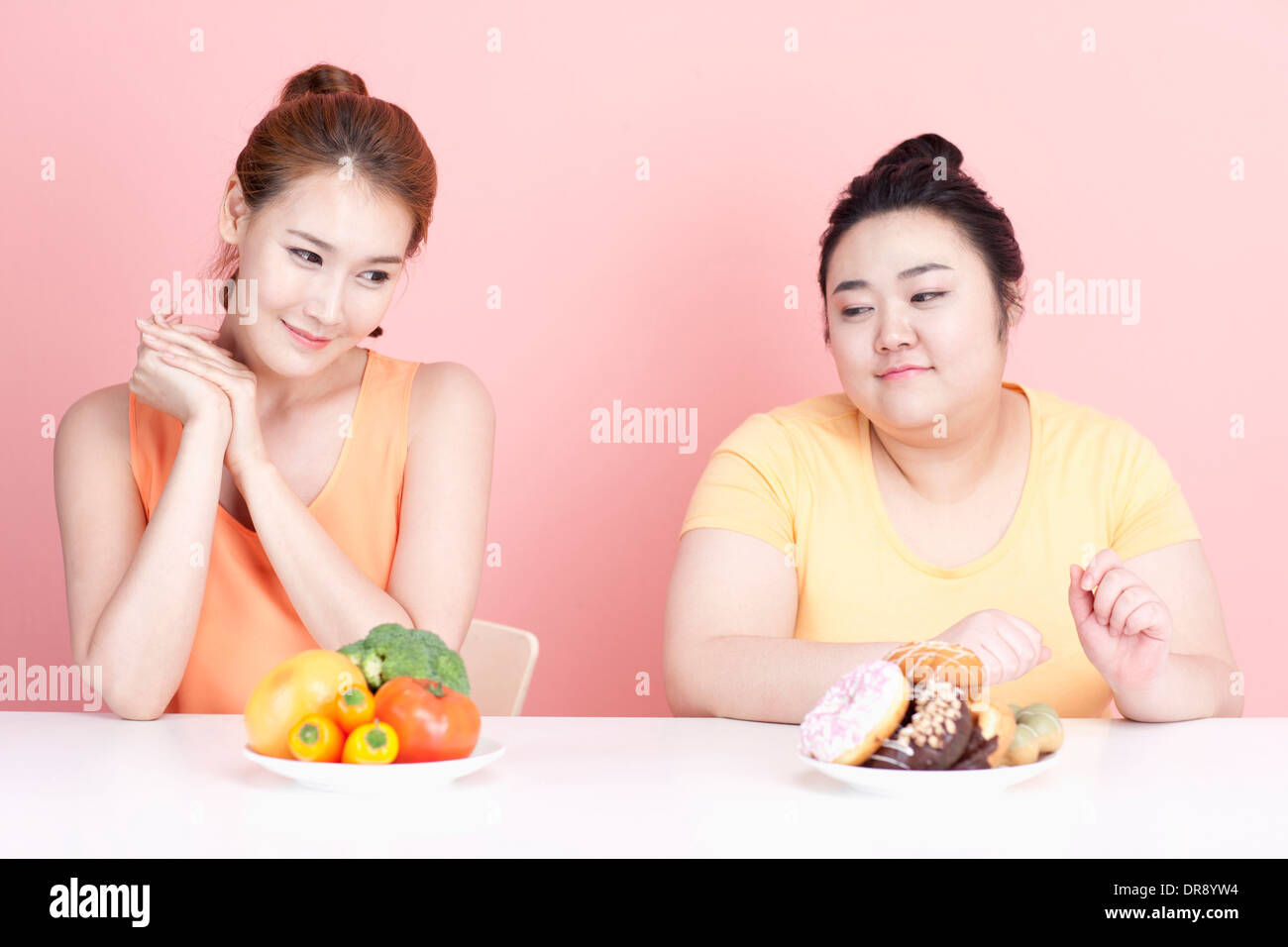 a thin and chubby woman sitting at table with different food in front Stock Photo