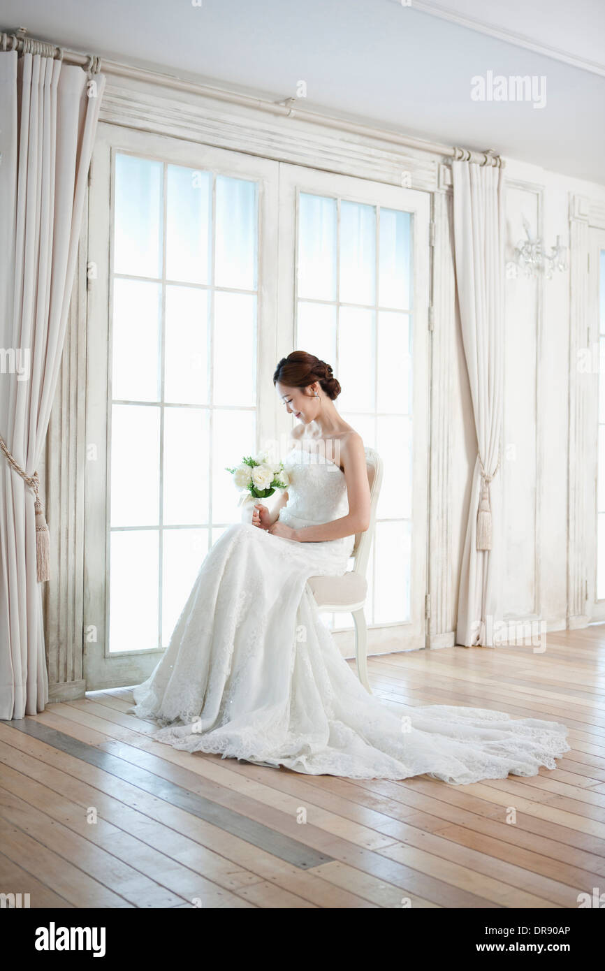 a woman sitting on a chair with wedding dress and flower bouquet Stock Photo