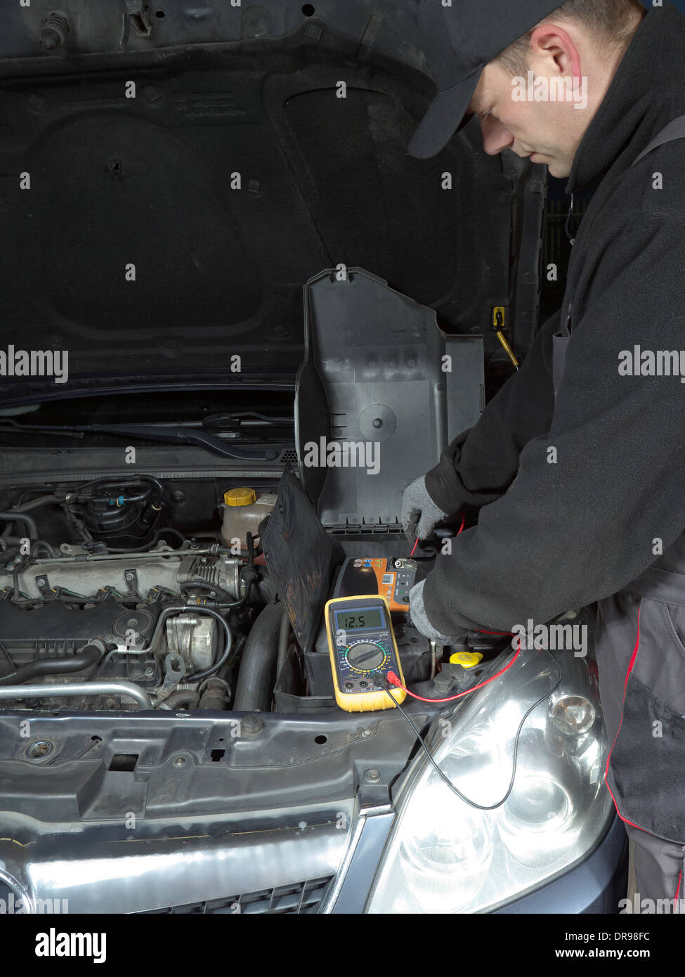 Auto mechanic measuring car battery voltage using multimeter Stock Photo