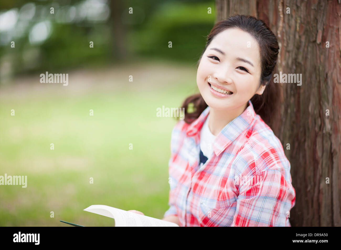 a woman leaning on tree reading a book Stock Photo