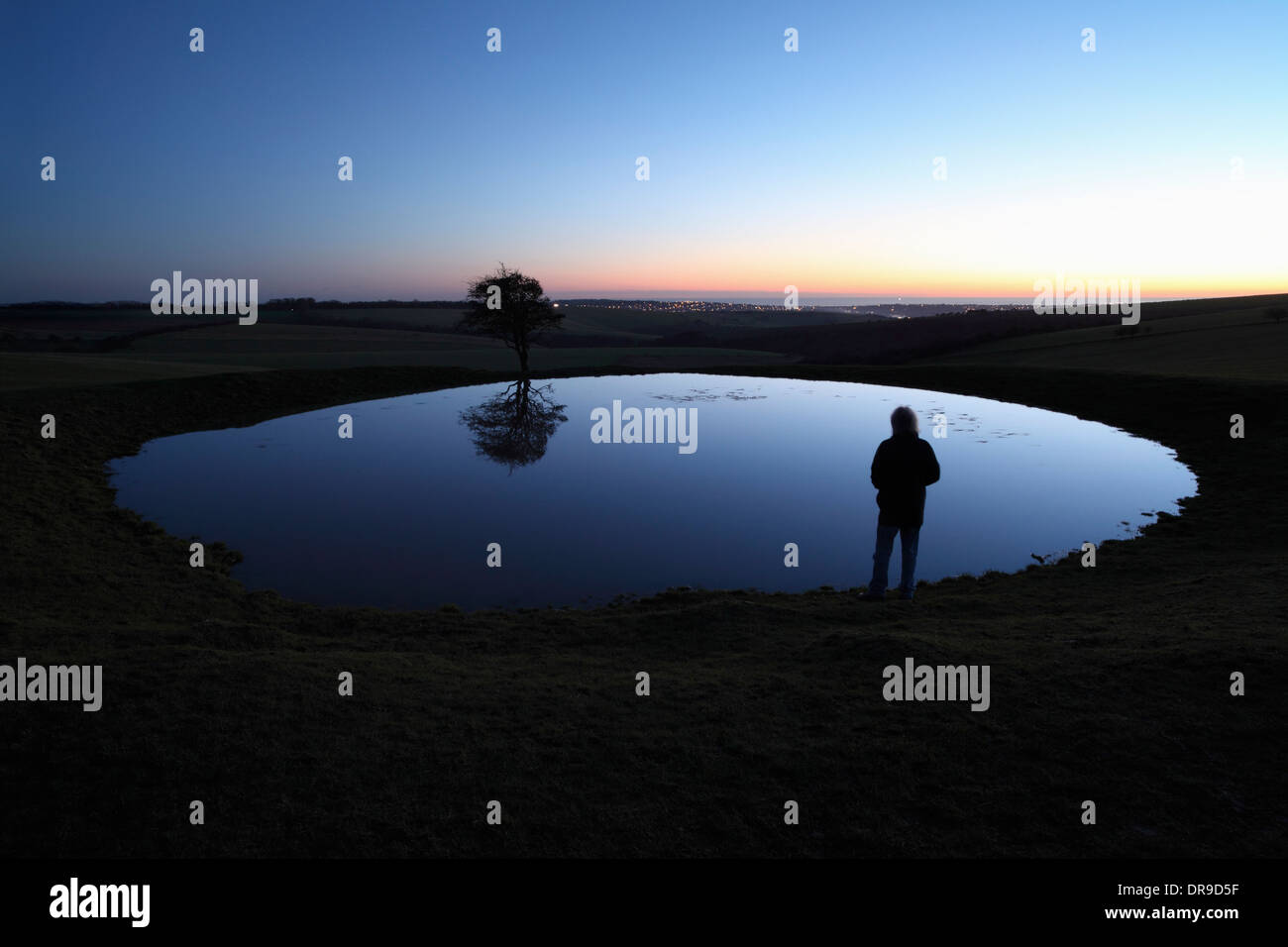 Man contemplating the meaning of life by a dew pond on the South Downs at dusk. Stock Photo