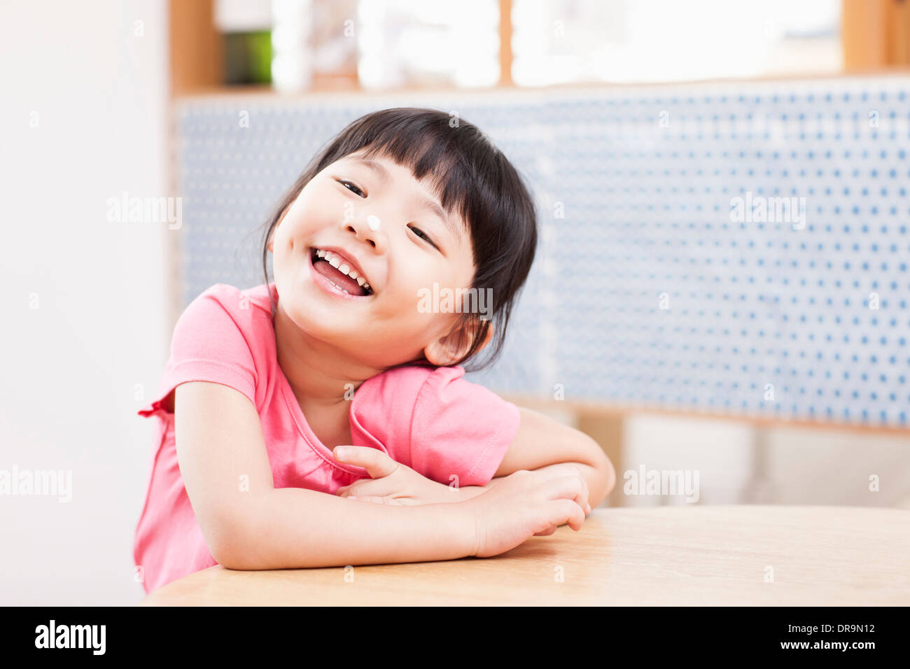 a girl sitting at a table smiling Stock Photo