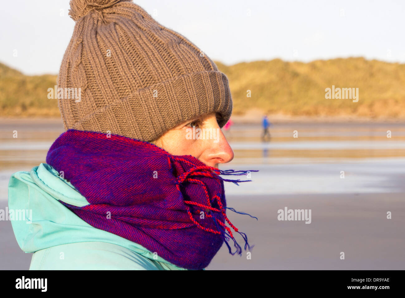 A woman wrapped up on the beach at Beadnell, Northumberland, UK. Stock Photo