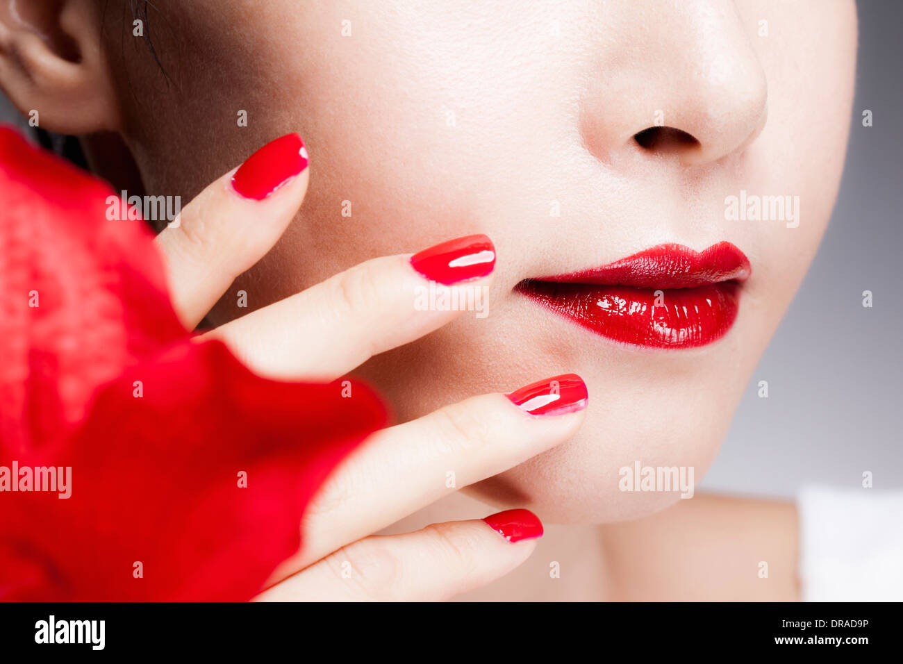 close up shot of a woman's red nails on a face with red lips Stock Photo