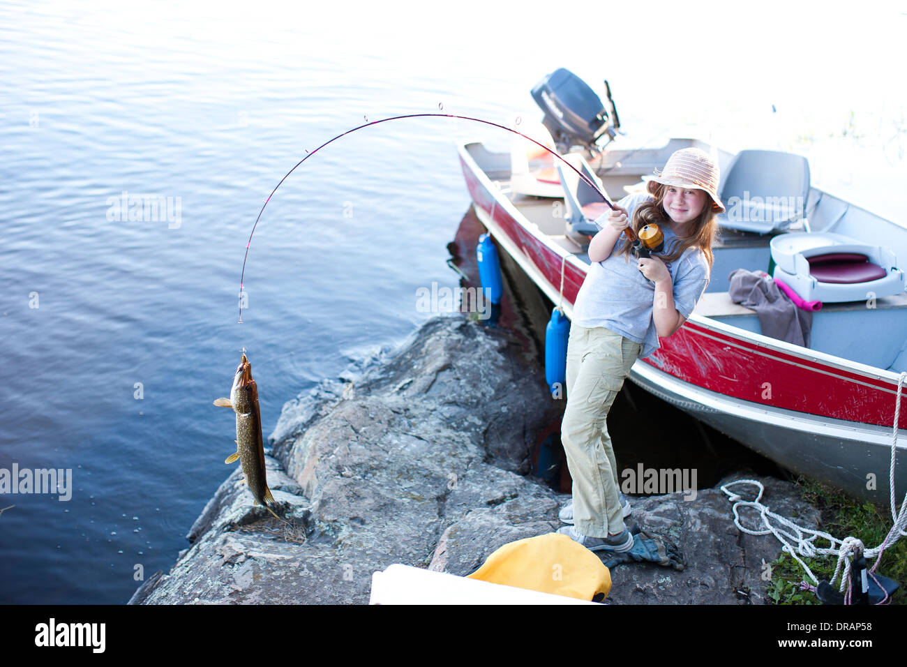 A little girl holds a fishing pole with a large fish on the end of